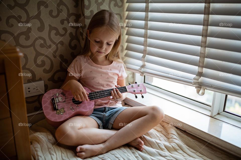 Little Caucasian girl playing on ukulele at home