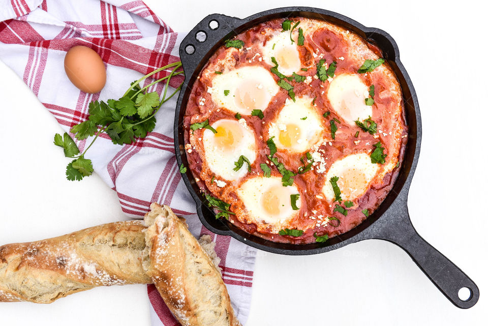 Flat lay of a shakshouka dish in a cast iron skillet next to a loaf of bread