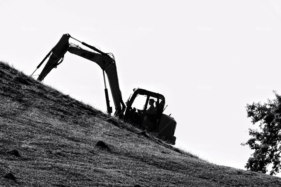 Silhouette of an excavator driving up a steep mountain in a meadow