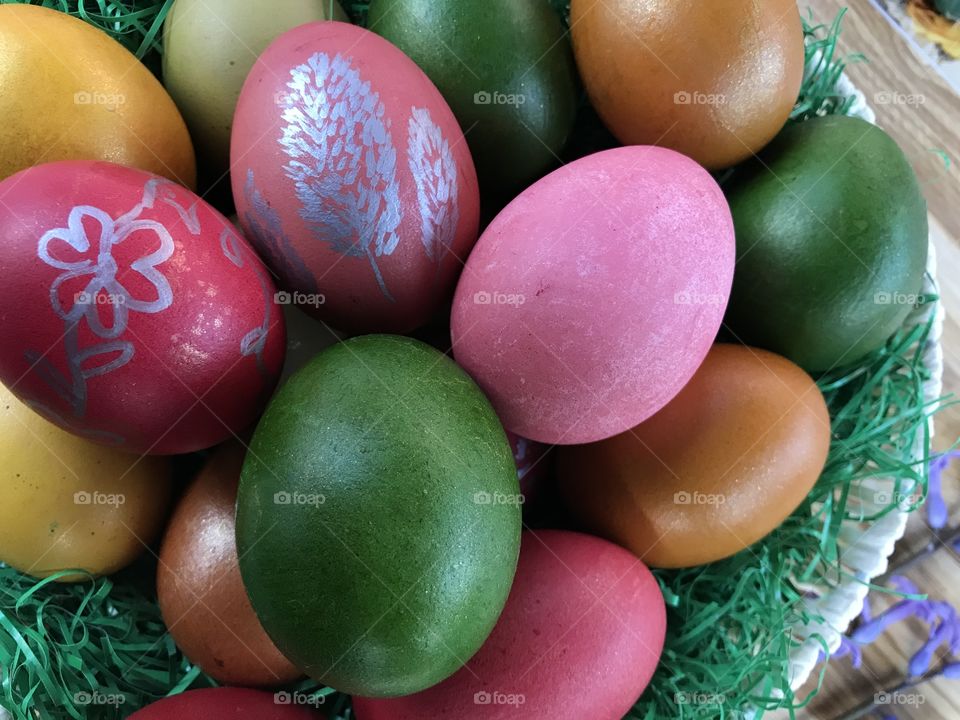 Colorful Easter eggs in pink, green, dark orange, light brown color in a basket with green grass.