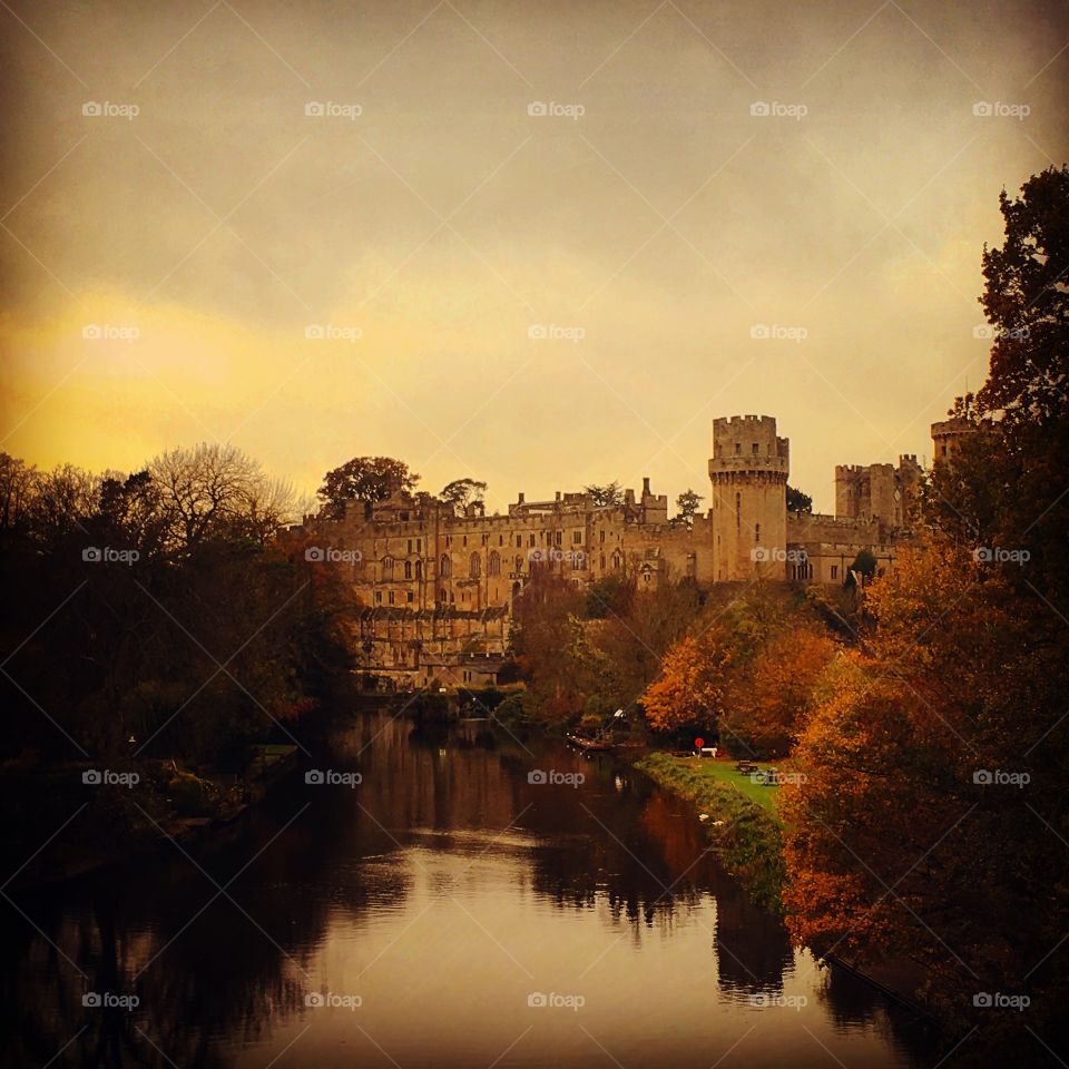 View of Warwick castle over a river, orange autumn sunset 