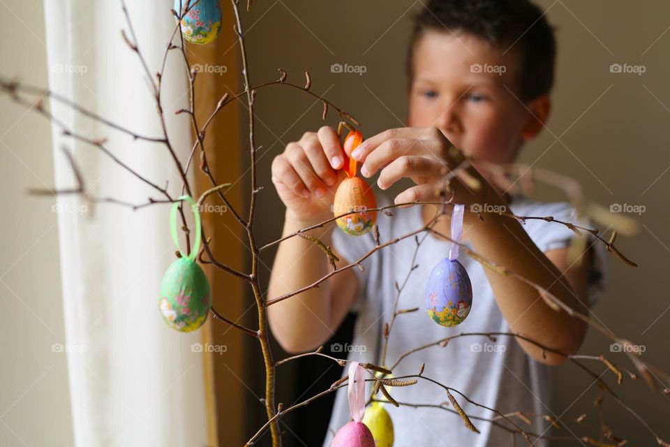 a boy of seven years old, paints crafts at home, Easter eggs, the boy is preparing for the holiday.  home crafts, craft activity.  a child decorates a tree branch with homemade eggs for Easter