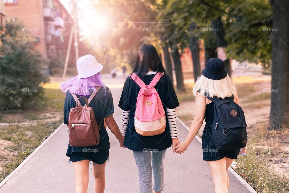 Three young hipsters students walking with backpacks by the autumn street together 