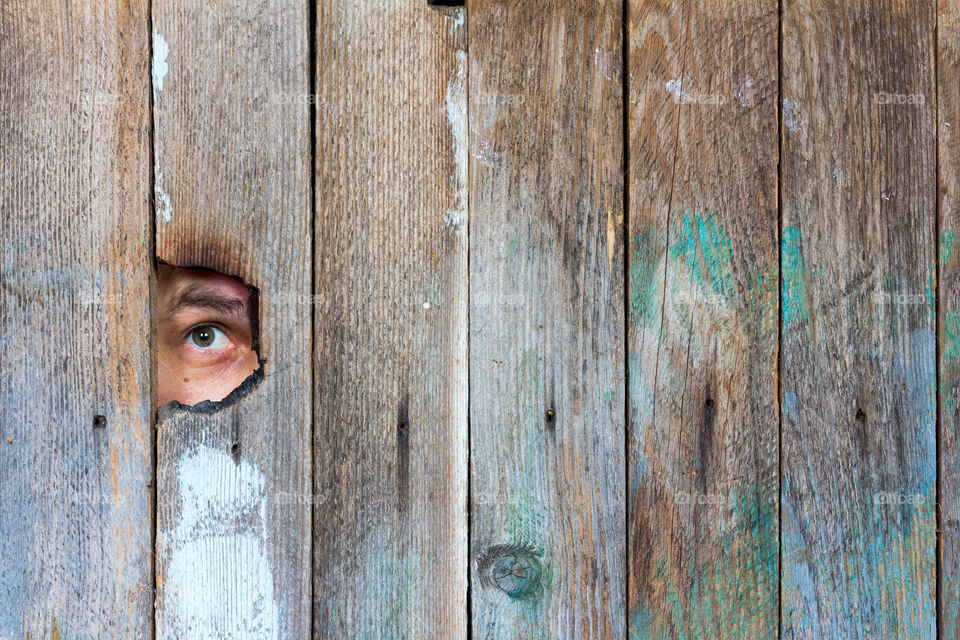 male eye looking into a hole in a wooden fence