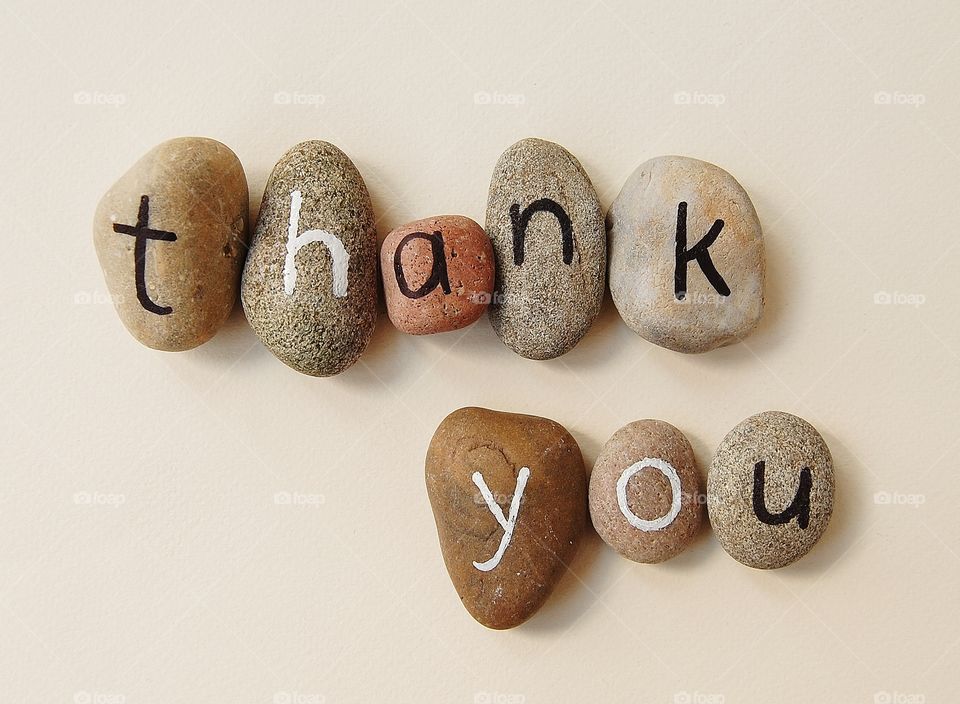 Thank you spelled in natural coloured stones with lowercase letters in black ink and white ink. 
