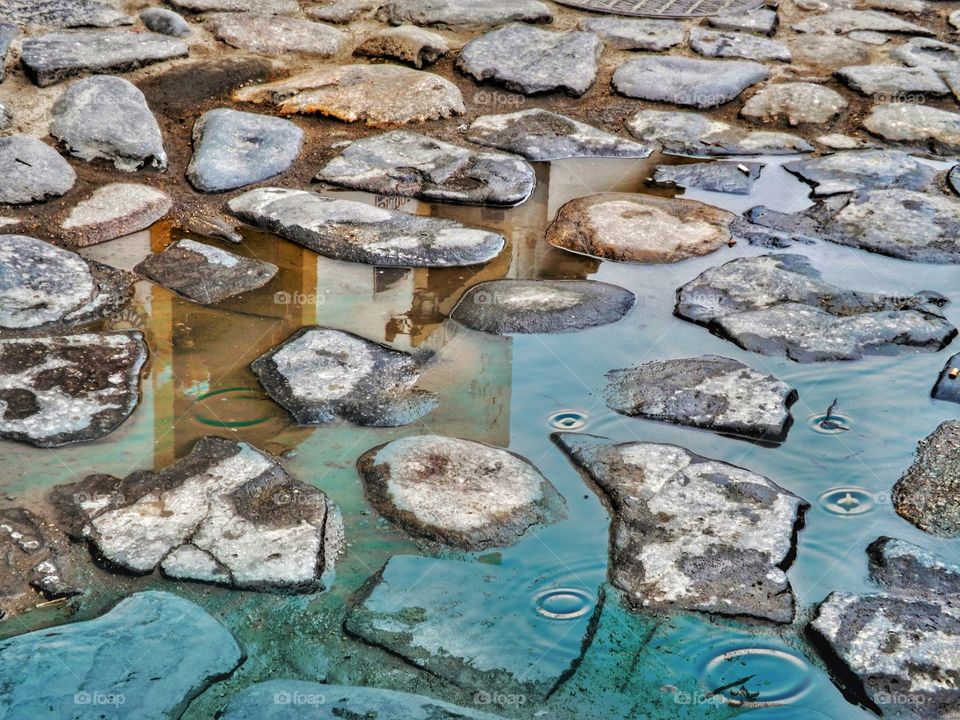 Raindrops in a puddle of water in a stone street