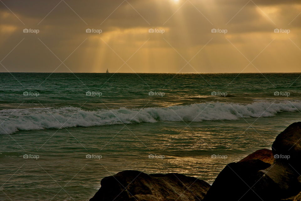 A boat sailing in the distance as the sun’s rays are trying to come through the clouds