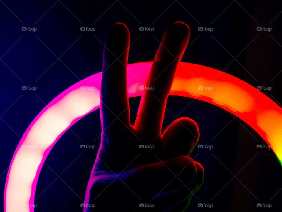 Hand making the peace symbol illuminated by colorful lights in the dark.