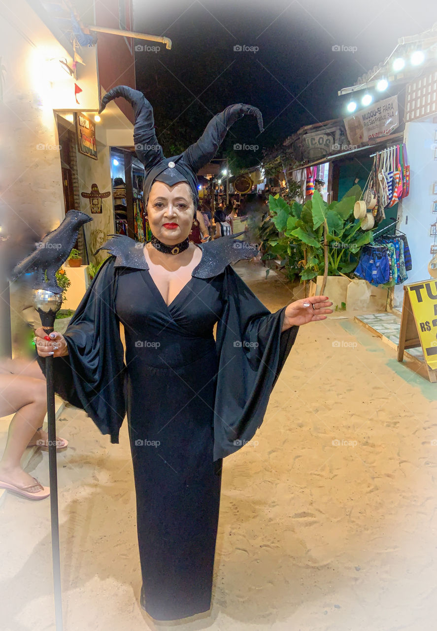 Black witch with black raven walking on the sand street 