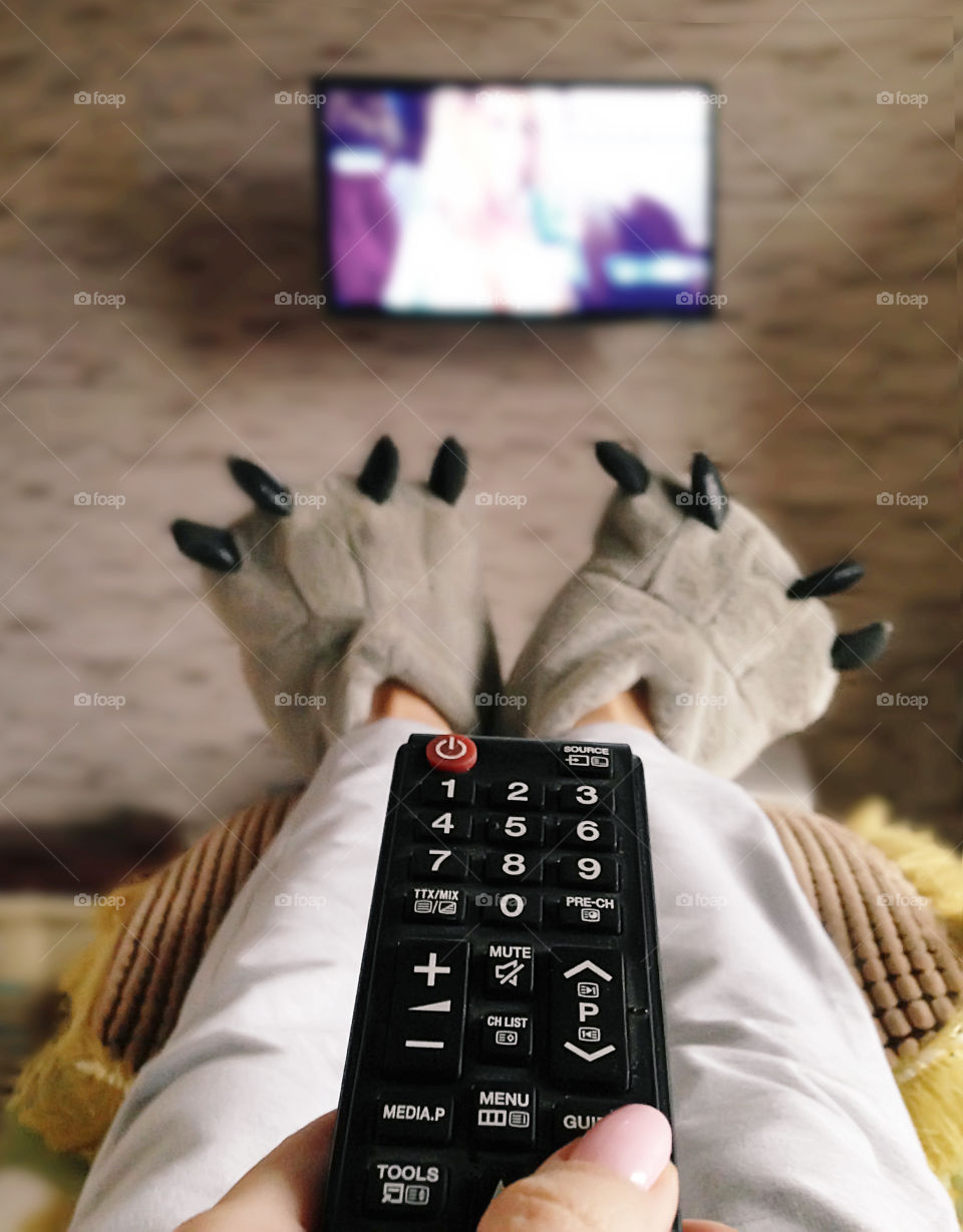 Watching television in funny home slippers in cozy bed with pillows during the quiet evening 