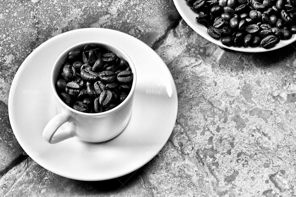 coffee beans in a white cup on stone floor background in black and white