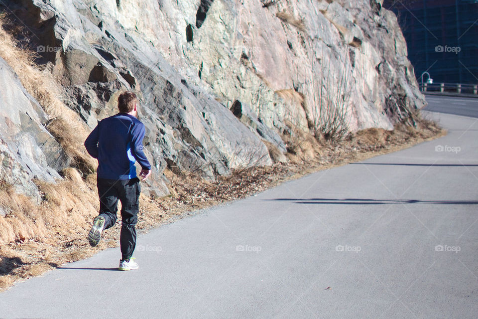 Man running on a biking trail alongside some cliffs
