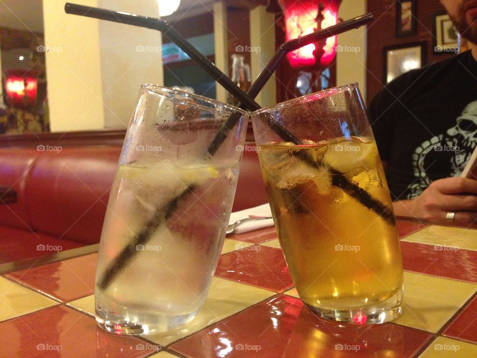 Kissing Drinks. Two glasses that lean into each other on a tiled table. 