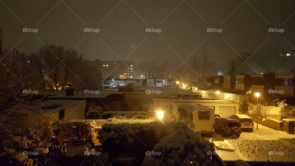 Snow at evening/night with yellow/orange lights from a Window.