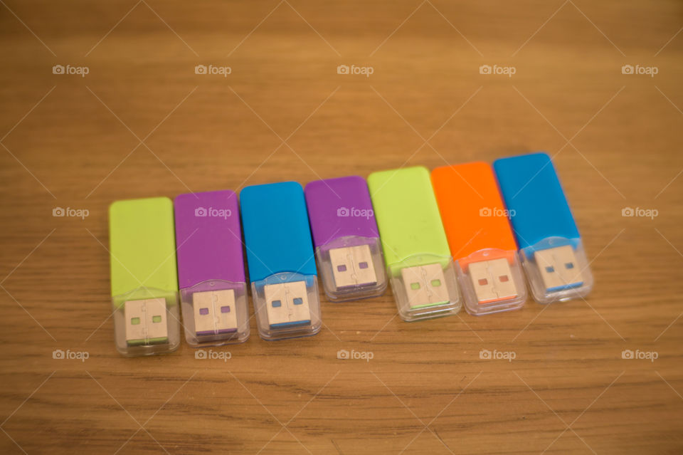 Multi-colored flash drives for working with documents, saving and transmitting, sharing files on a wooden texture table close-up.