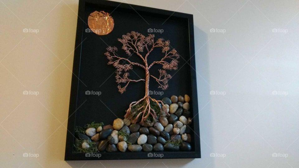 A copper wire and tumbled stone art piece depicting a tree and the sun.