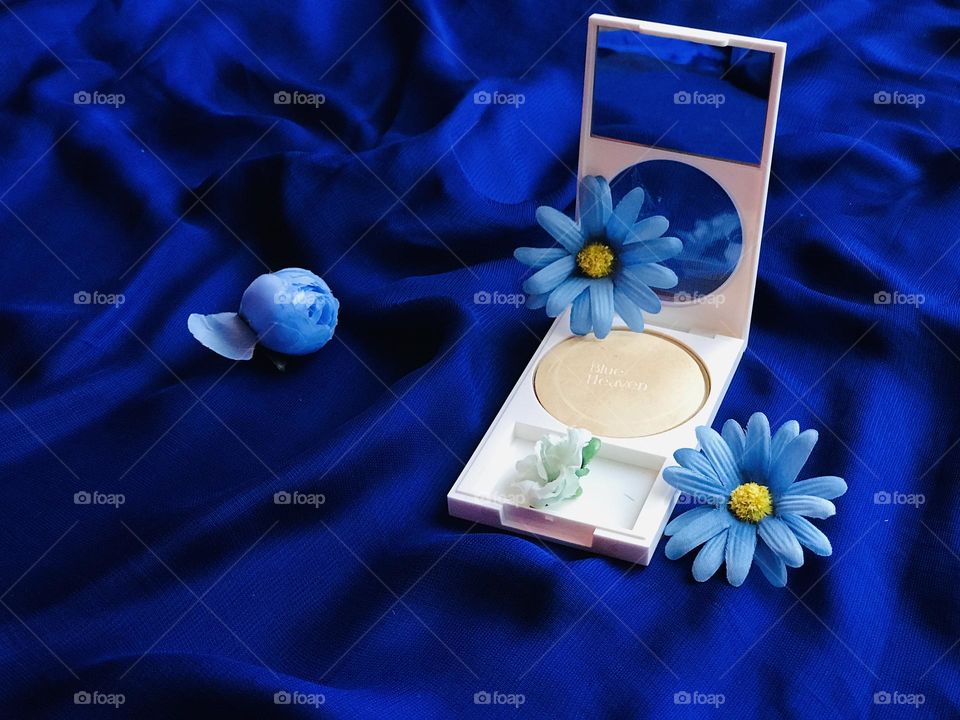 Blue heaven foundation powder along with blue flowers on blue satin cloth 