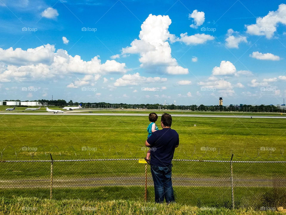 Father and son observing from the overlook at the Charlotte Douglass International Airport as airplanes taxi and take off from the runway.