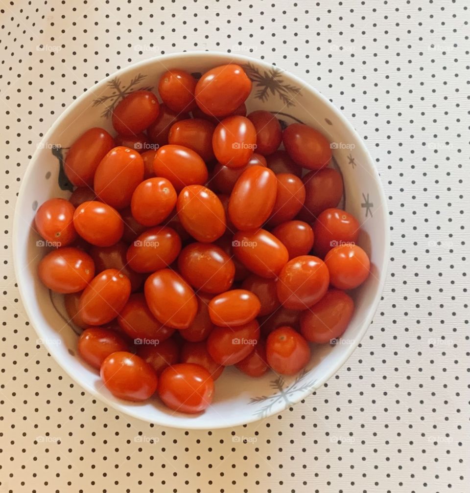 Red cherry tomatoes in a bowl and polka dot background 