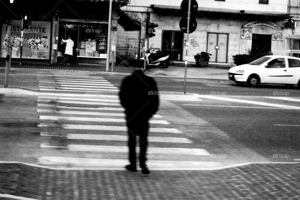 Man wearing all black passing the street headed to the pharmacy, black and white photo, white geometric shapes, zebra crossing connects the subject with the guy in the white coat