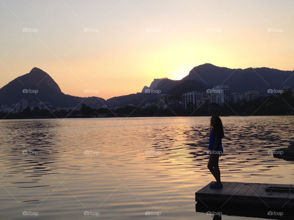 A girl watching the sunset at the edge of a lake,in Rio de Janeiro 