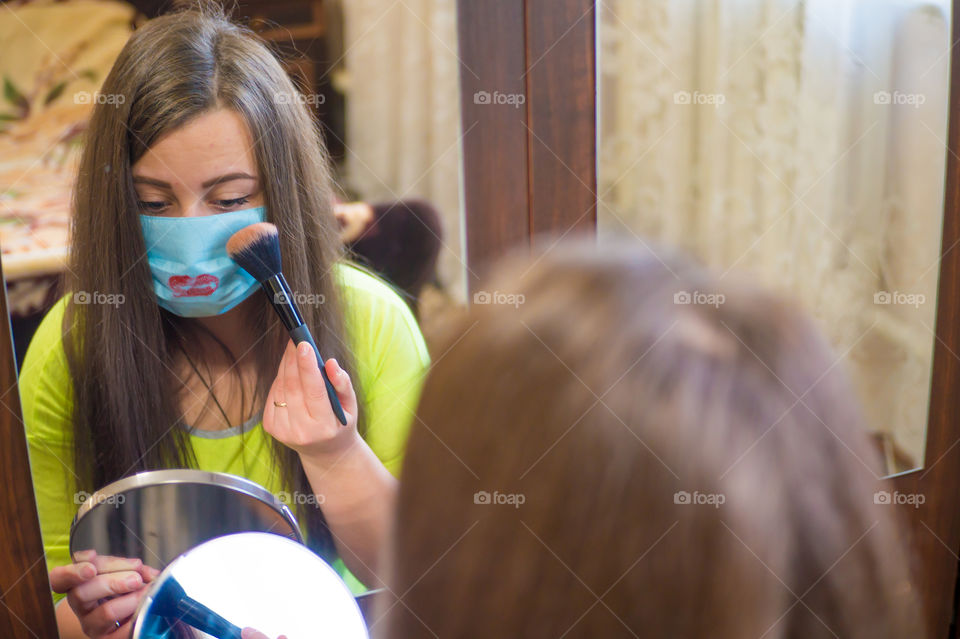 A young girl does makeup for a walk outside in a protective mask against the coronavirus pandemic, her lips are painted with red lipstick.