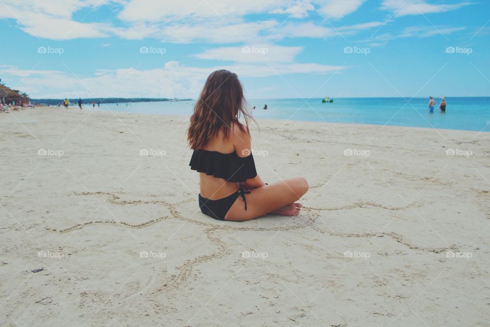 Girl sitting on the beach facing the water
