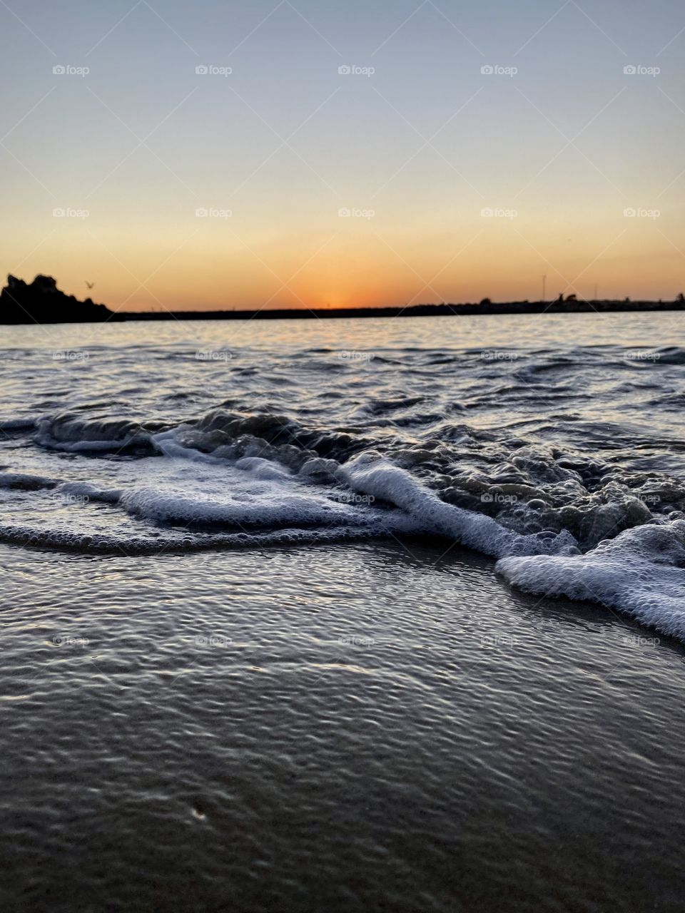 Sunset at Pirates Cove Beach with a wave crashing on shore 