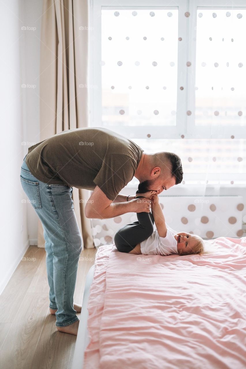 Young happy family with father and daughter baby girl on bed in cozy home