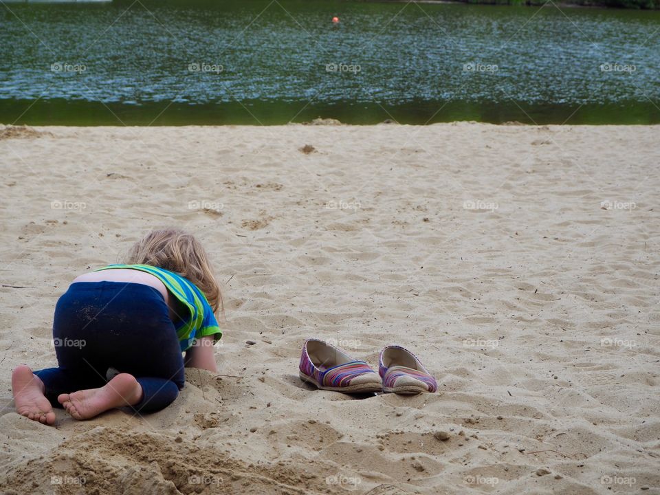 Child on beach next to adult shoes