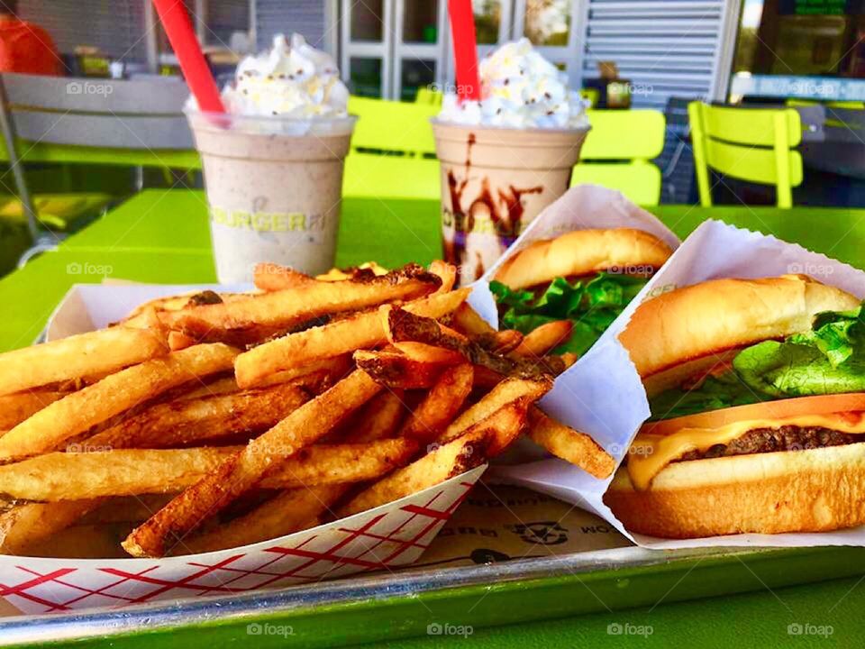 Platter with delicious cheeseburgers, fries and milkshakes with whipped cream