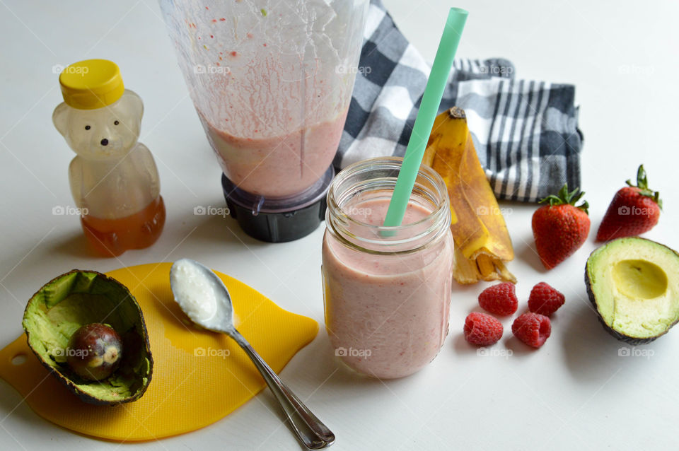 Fresh fruit smoothie in a glass with banana peel, strawberries, raspberries, avocado, and honey bear