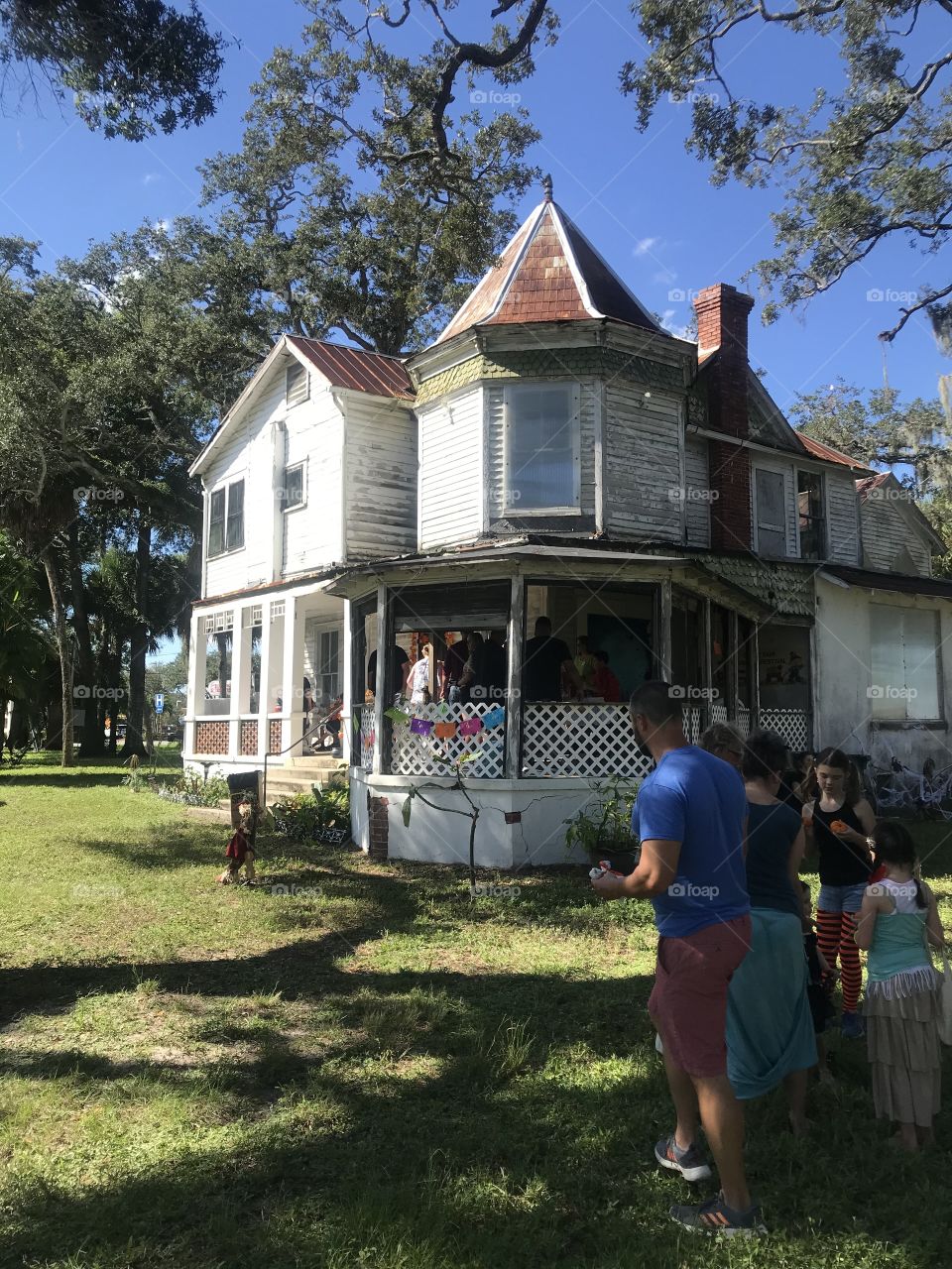 An old white 2-story house with a porch and a turret 