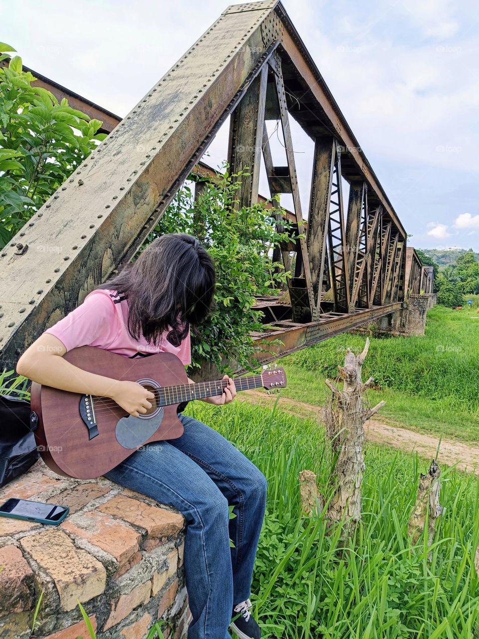 A girl  was playing the guitar near the old iron railway bridge.