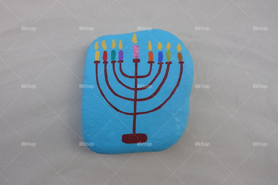 Symbol of jewish holiday Hanukkah with a painted stylized design of a Menorah, candlestick with nine candles over a stone