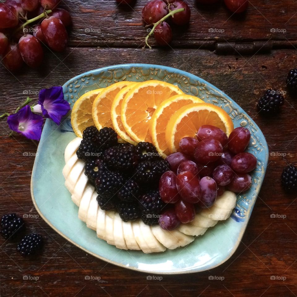 Fresh fruit platter with oranges, grapes, blackberries and sliced banana on a wooden table.
