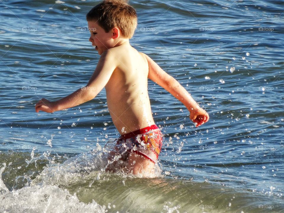 Little Boy Challenging The Ocean. Splashing Boy
