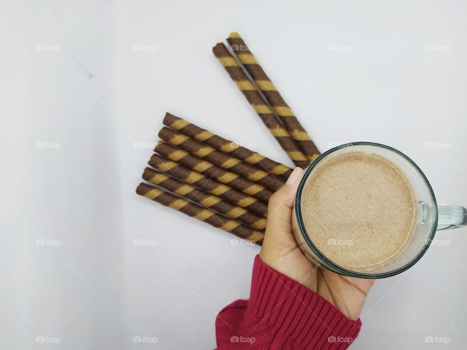 Holding a glass of chocolate milk and some wafer roll sticks on white background. Top view