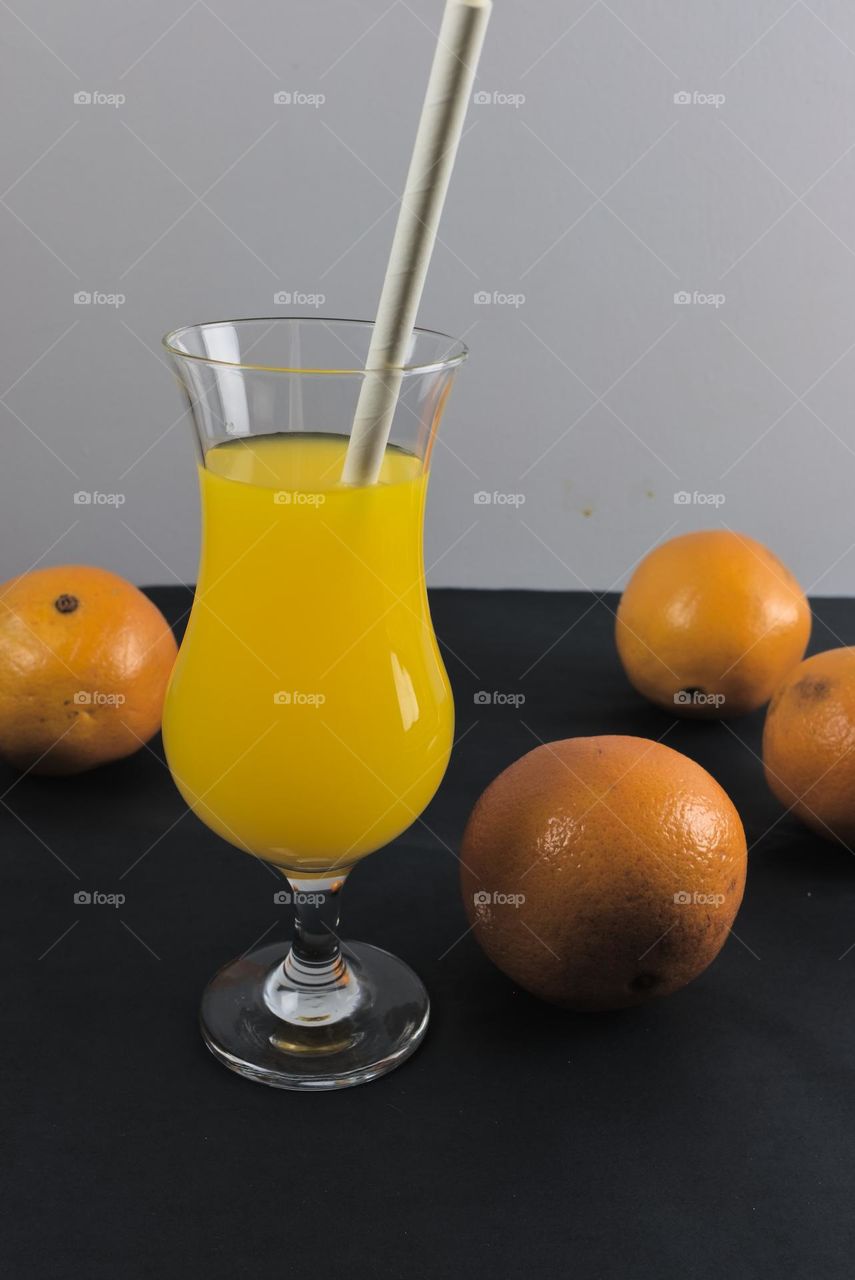 Oranges and glass tumbler with orange juice on black background