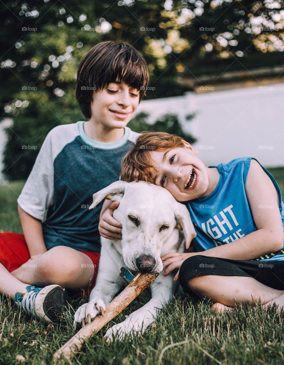 Brothers sitting on the grass outside with their dog 