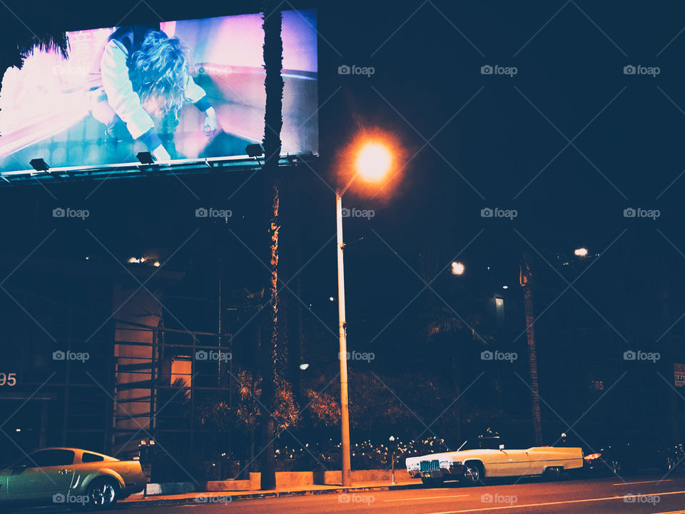 Sunset Blvd in Los Angeles California a dirty white Cadillac sits under a neon billboard and lit by one lone street light