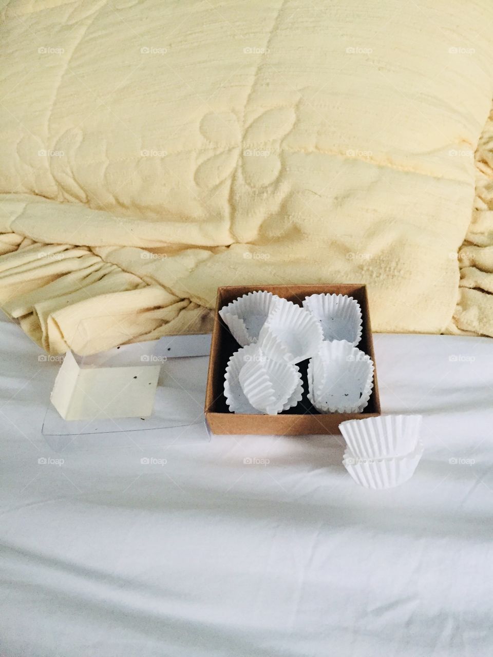 An empty box of chocolates with the wrappers scattered on a bedspread. There’s a yellow pillow in the background.