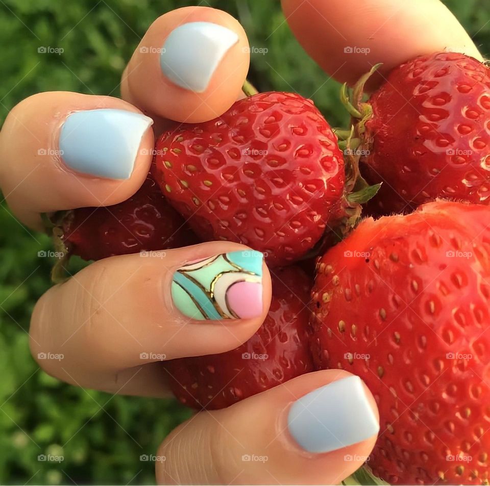 female hands with beautiful blue manicure and color drawing, holding strawberries