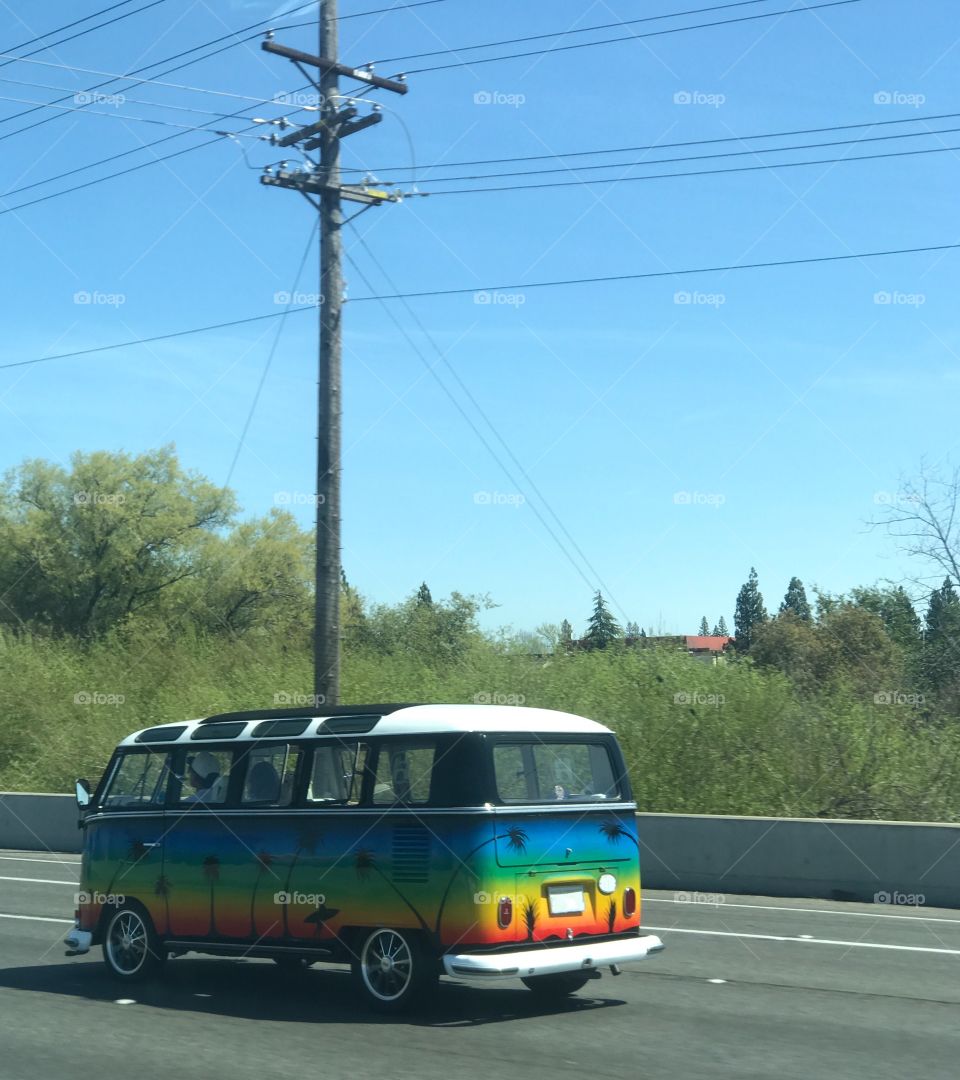 A tie-dye psychedelic colored Volkswagen hippy van driving on the freeway outside. USA, America 