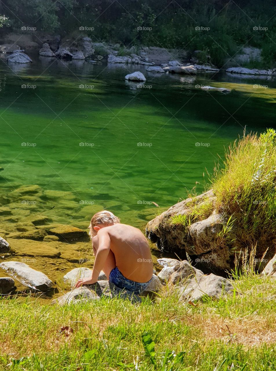 a boy sitting by the river shore