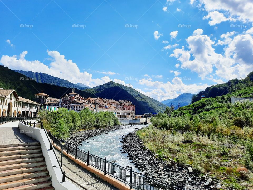Summer bright day in mountain town, river Mzymta embankment, stairs, green, nature and modern buildings around