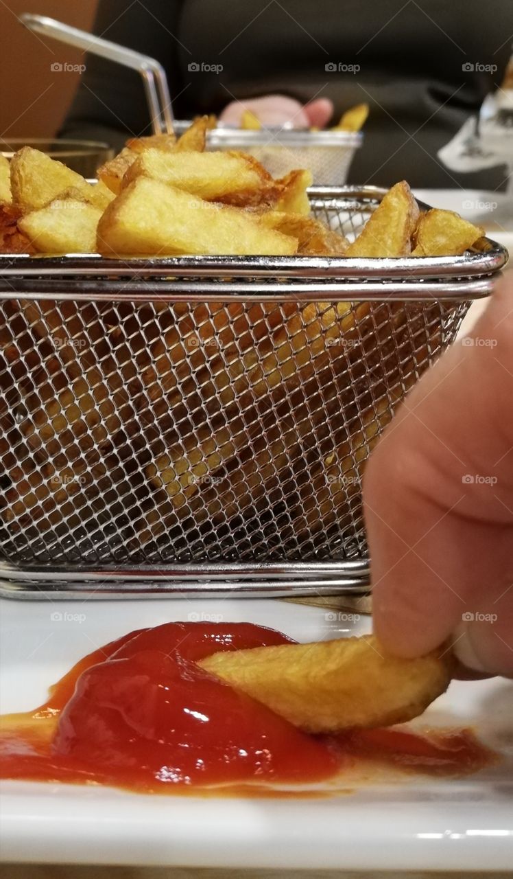 The French fries in the metallic basket. A piece of the chips dipped in the ketchup.