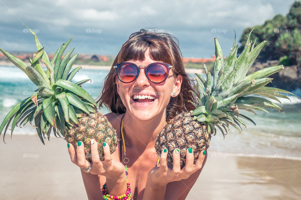 The girl laughs and holds pineapples in her hands. Bali island, Nusa-Dua beach.