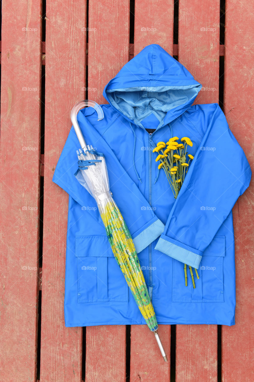 Flat lay of a blue raincoat with a bouquet of flowers and an umbrella
