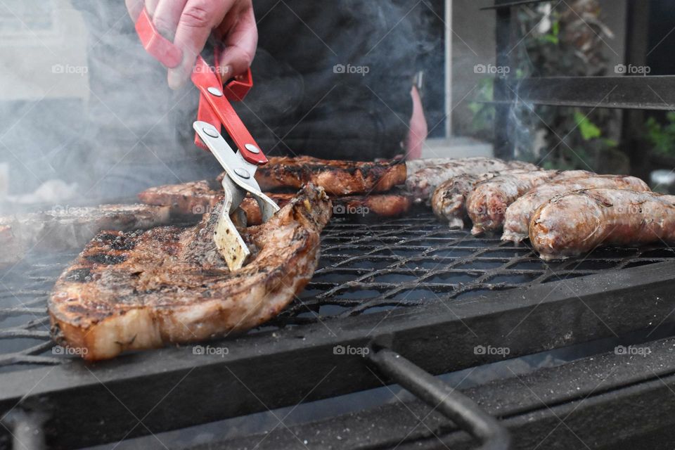 Backyard barbecue and Braai. Man braai barbecue sausages, food meat at home in the yard. Men grilling lots of meat on steel grill. Braai steak pork chops sausages and braai bacon. Cooking at home and outdoor cooking. Make a hotdog in bun bread roll.